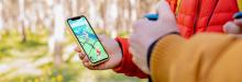 Two people play Pokemon Go at a park. By highlighting the game’s map interface, we see how users can explore their city through play. The embedded digital landmark on the phone illustrates how the app gamifies public spaces.